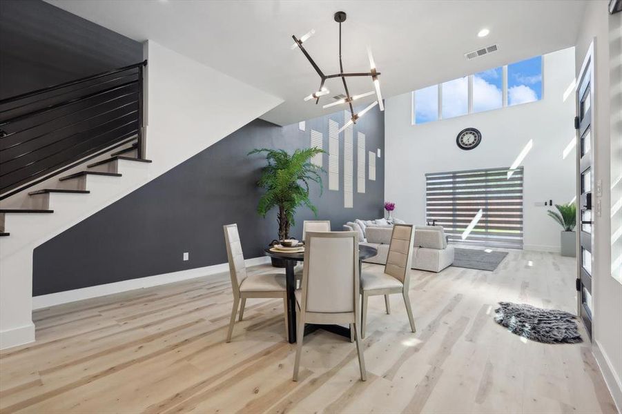 Dining room with light hardwood / wood-style floors, an inviting chandelier, a healthy amount of sunlight, and a high ceiling