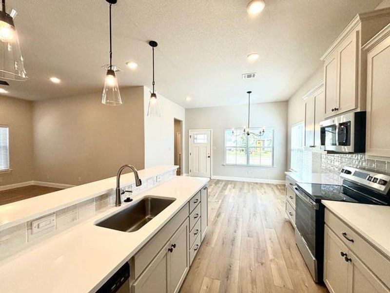 Kitchen with sink, decorative light fixtures, light hardwood / wood-style flooring, appliances with stainless steel finishes, and a notable chandelier