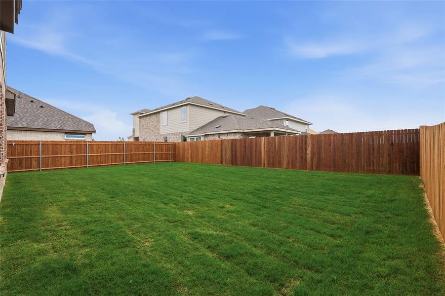 Spacious backyard featuring a lush green lawn, full wood privacy fencing, and brick exterior detailing