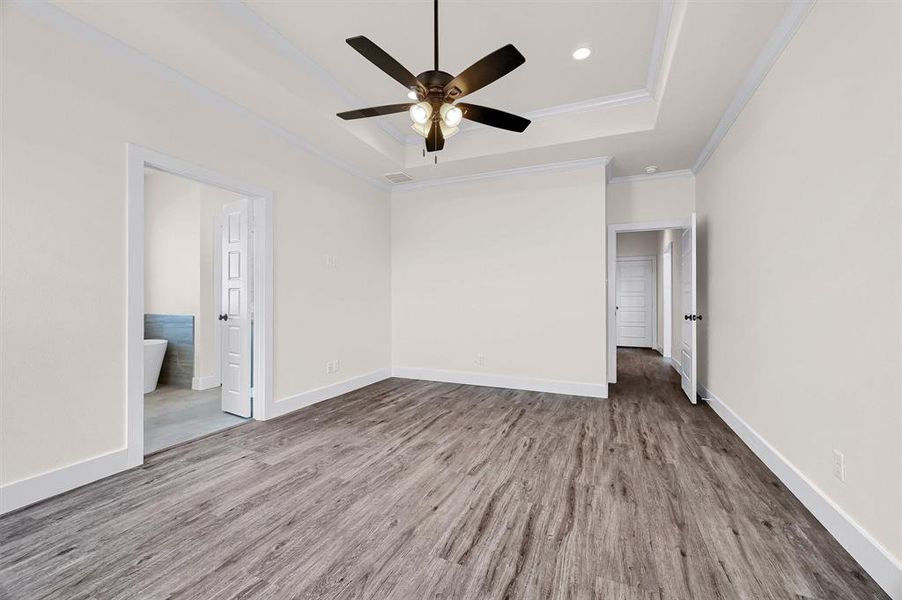 Empty room featuring ceiling fan, ornamental molding, a tray ceiling, and wood-type flooring