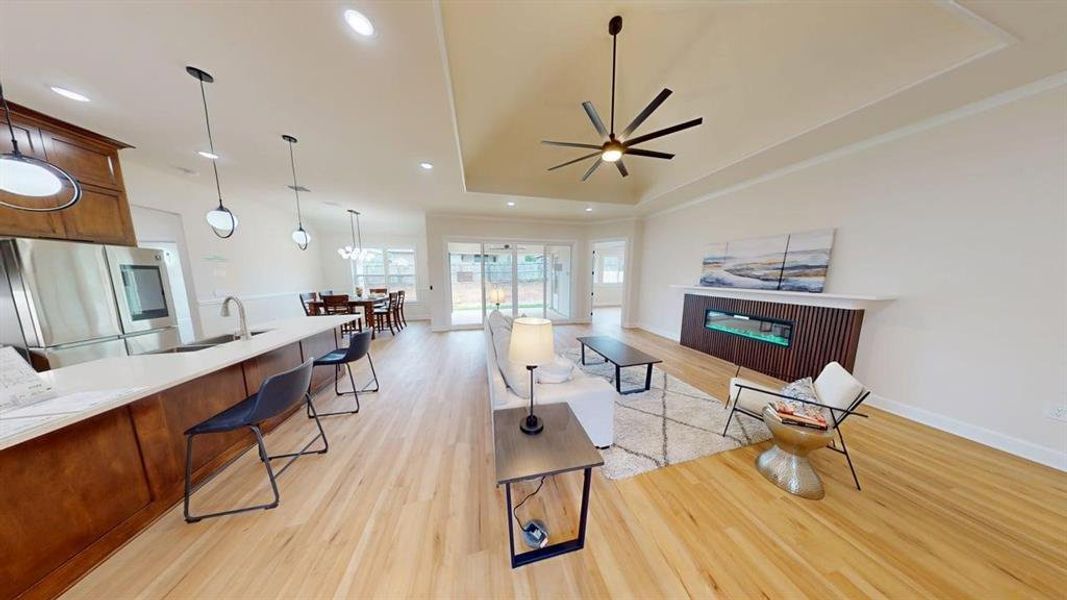Living room featuring light wood finished floors, a raised ceiling, ceiling fan, a fireplace, and recessed lighting