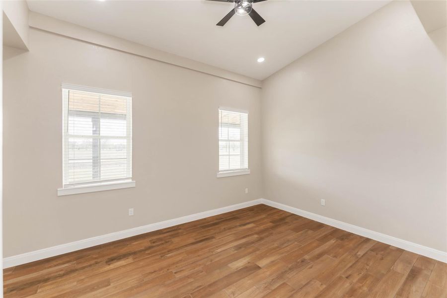 This room features a spacious layout with high ceilings, tile wood-style flooring, taupe walls, and ample natural light from two large windows. A ceiling fan adds comfort to the space. Perfect for a bedroom or home office.