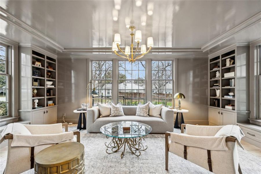 Living area featuring built in features, a healthy amount of sunlight, crown molding, and a notable chandelier