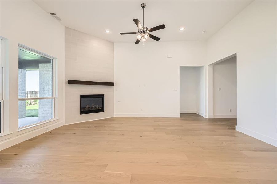 Unfurnished living room with a large fireplace, light hardwood / wood-style flooring, and ceiling fan