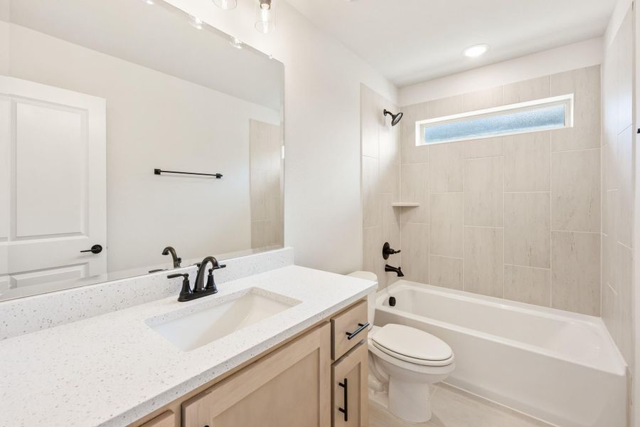 Bathroom with quartz countertop vanity, tub-shower combo with tile surround, and black hardware fixtures