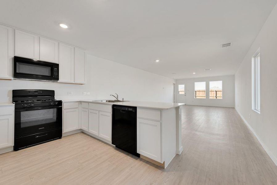 Kitchen featuring black appliances, a peninsula, white cabinets, light countertops, and light wood finished floors