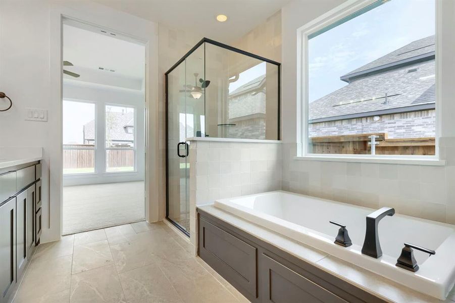 Bathroom featuring a built-in soaking tub with dark-toned fixtures, a walk-in shower with black-framed glass enclosure, and a vanity with dark cabinetry Bathroom featuring a built-in soaking tub with dark-toned fixtures, a walk-in shower with black-framed glass enclosure, and a vanity with dark cabinetry