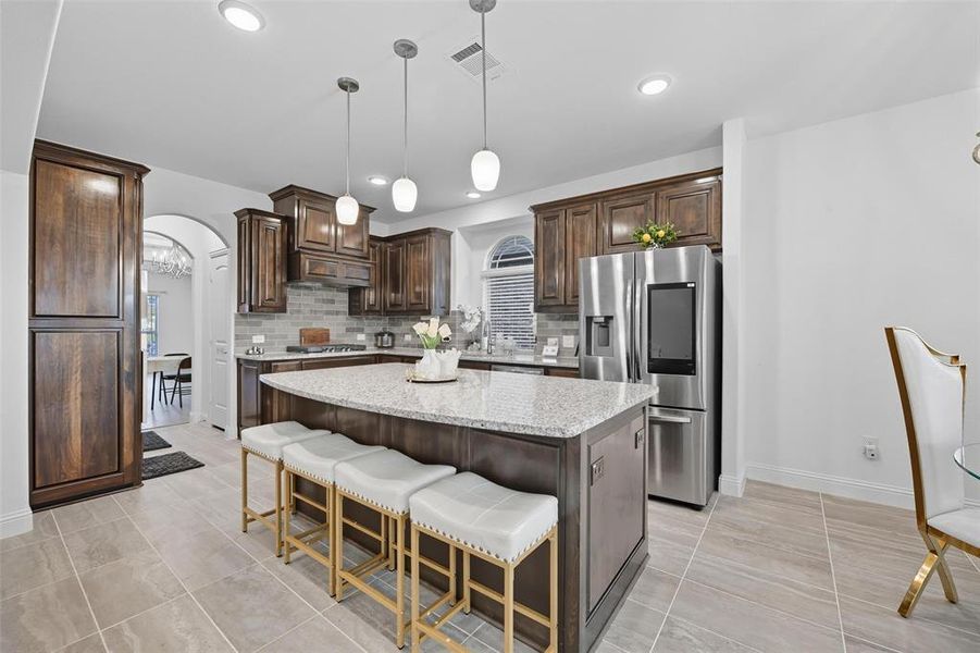 Kitchen featuring dark brown cabinets, arched walkways, a kitchen bar, a center island, and backsplash Kitchen featuring dark brown cabinets, arched walkways, a kitchen bar, a center island, and backsplash