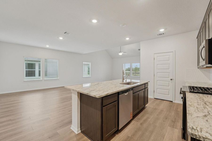 Kitchen featuring open floor plan, light stone countertops, light wood finished floors, a kitchen island with sink, and recessed lighting