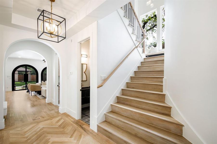 Entryway featuring a wood-finish herringbone floor pattern, an arched doorway, and an overhead geometric light fixture Entryway featuring a wood-finish herringbone floor pattern, an arched doorway, and an overhead geometric light fixture