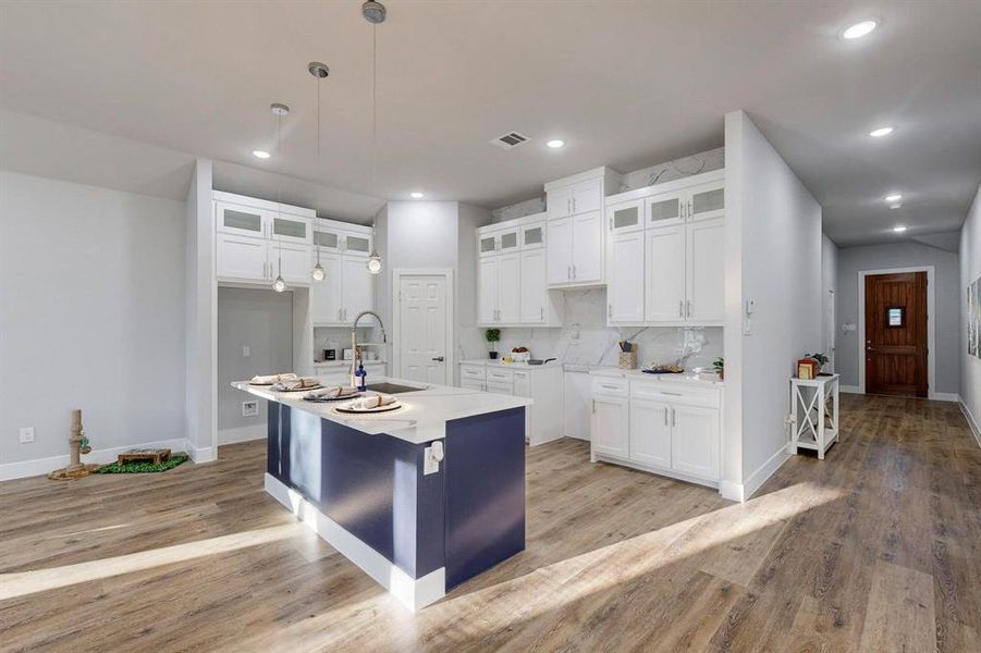 Kitchen with sink, a kitchen island with sink, hanging light fixtures, tasteful backsplash, and white cabinets