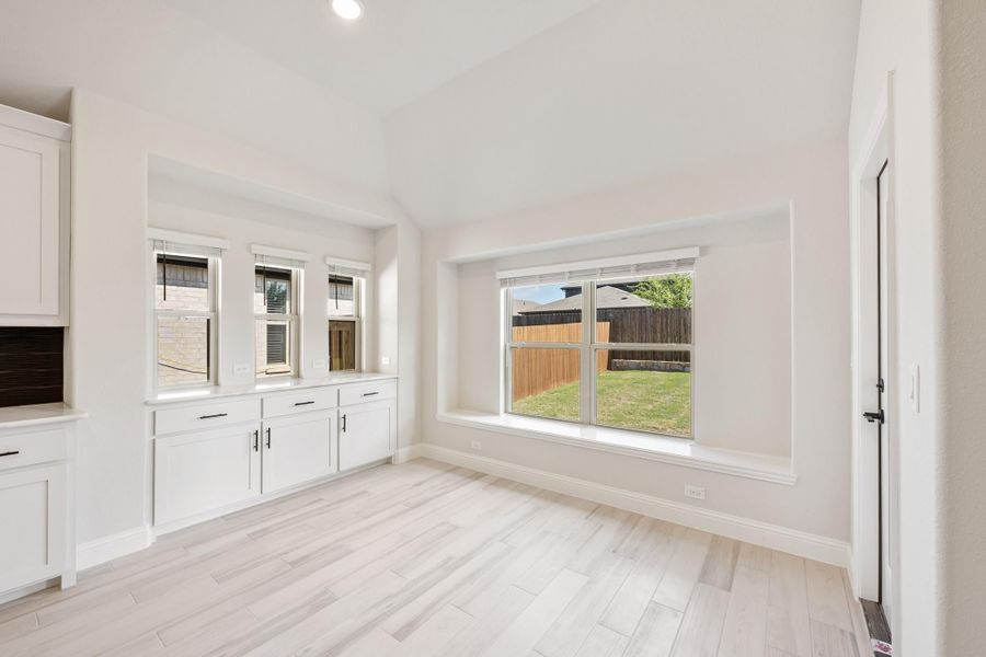 Bright dining area with white built-in cabinets, large windows, and light wood-look floors overlooking a backyard Bright dining area with white built-in cabinets, large windows, and light wood-look floors overlooking a backyard