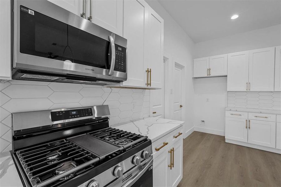 Kitchen with stainless steel appliances, tasteful backsplash, light stone countertops, white cabinetry, and wood finished floors Kitchen with stainless steel appliances, tasteful backsplash, light stone countertops, white cabinetry, and wood finished floors