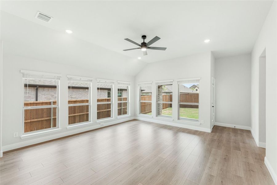 Bright open living room with vaulted ceiling, ceiling fan, hardwood floors, and large windows overlooking backyard