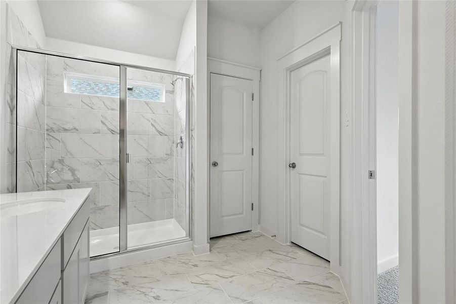 Full bath with a shower stall, vanity, and marble look tile flooring