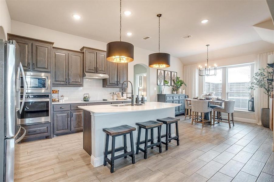 Kitchen featuring stainless steel appliances, sink, light hardwood / wood-style floors, hanging light fixtures, and an island with sink