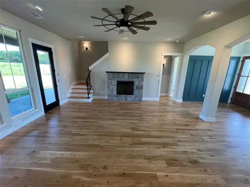 Spacious living area featuring wood-finish flooring and a stone-faced fireplace with a dark mantel