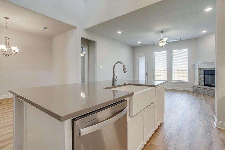 Kitchen with a stone fireplace, dishwasher, light wood-type flooring, and white cabinets