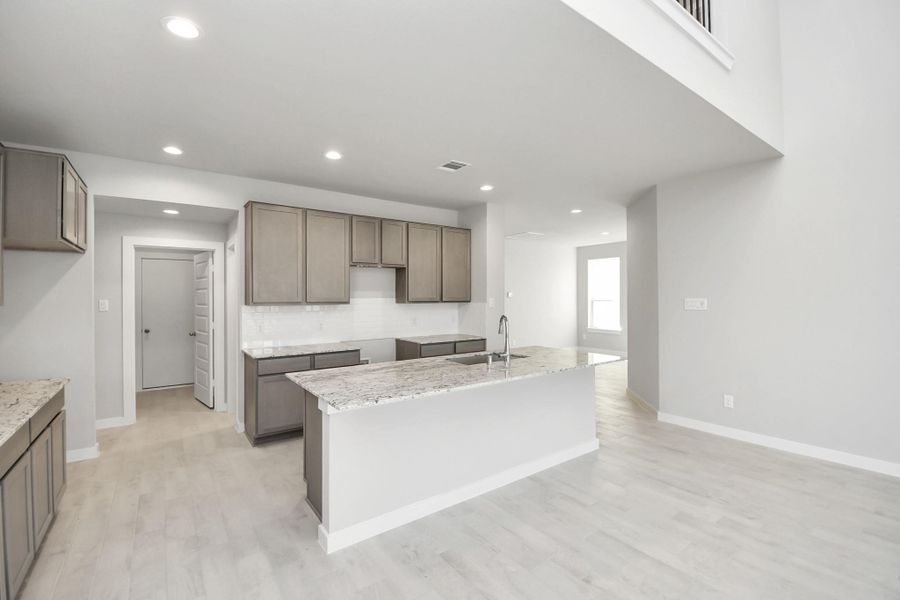 Discover another perspective of this stunning kitchen, sleek back splash, single basin sink, and generously appointed with an abundance of counter space. Sample photo of completed home with similar floor plan. Actual colors and selections may vary.