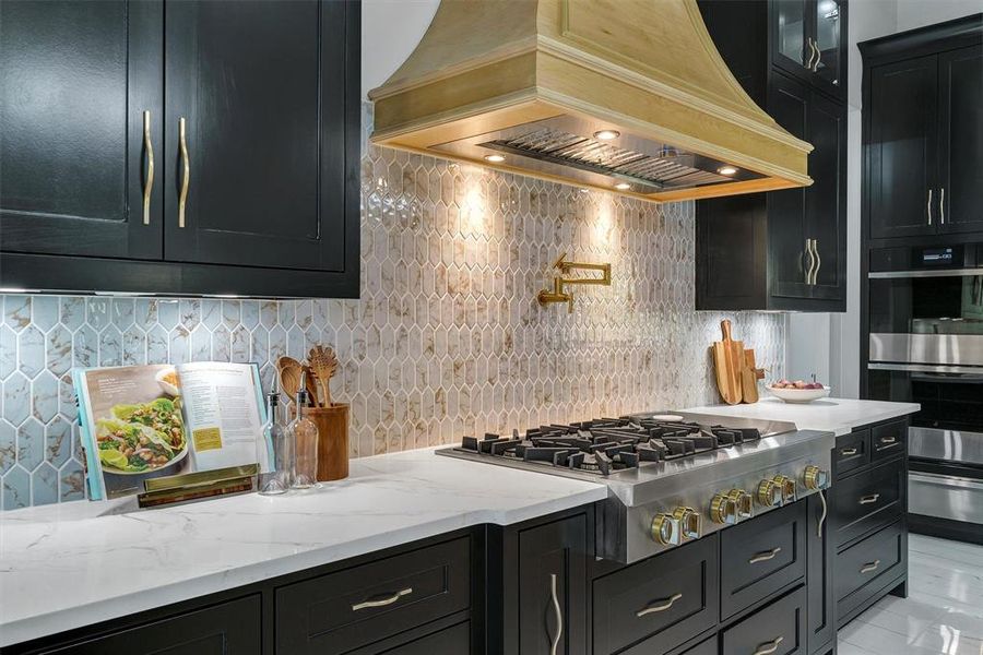 Kitchen with backsplash, light tile patterned floors, appliances with stainless steel finishes, light stone counters, and custom exhaust hood