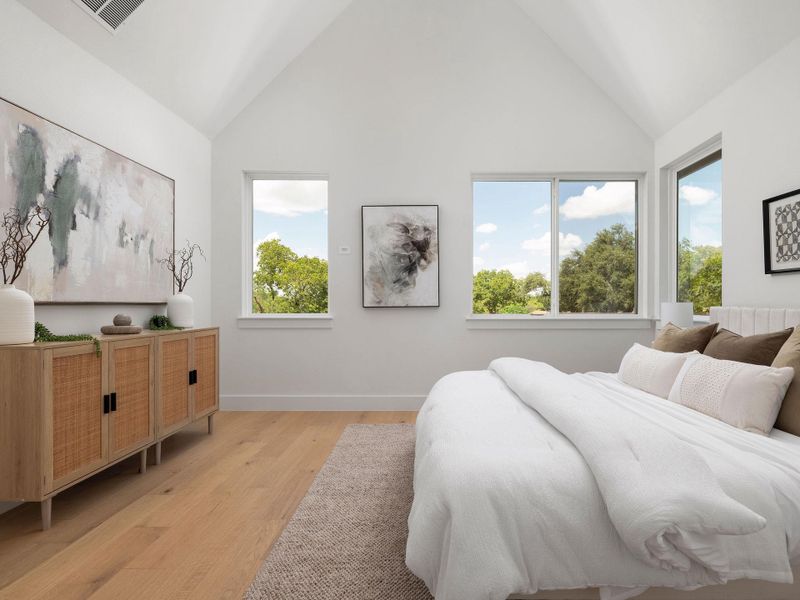 Natural light floods this primary bedroom with elegant vaulted ceilings and rich hardwood flooring.