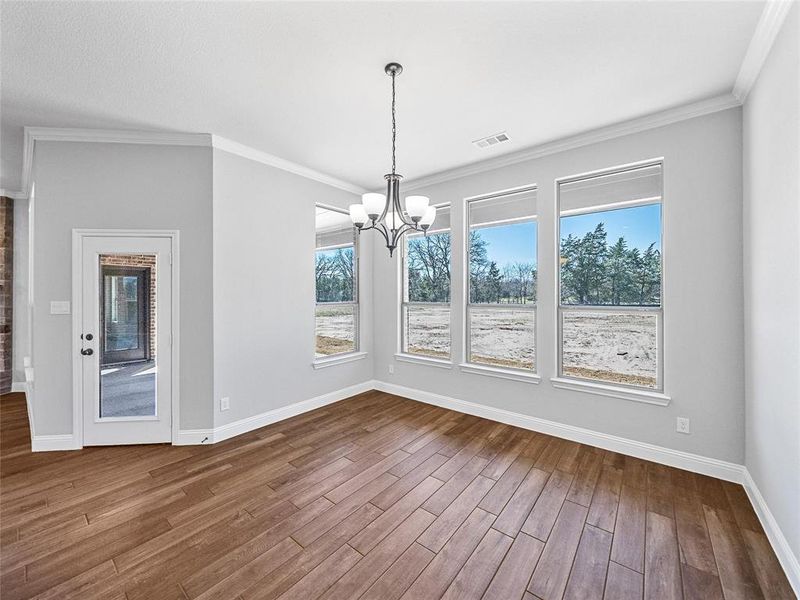 Prior listing photo. Property remains accurate - Unfurnished dining area featuring suspended lighting, dark wood finished floors, crown molding, and healthy amount of natural light