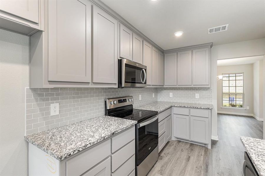 Kitchen featuring gray cabinetry, backsplash, light wood-type flooring, light stone countertops, and stainless steel appliances