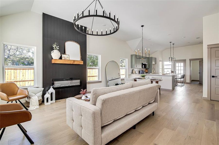 Living room with a chandelier, light wood-type flooring, and high vaulted ceiling