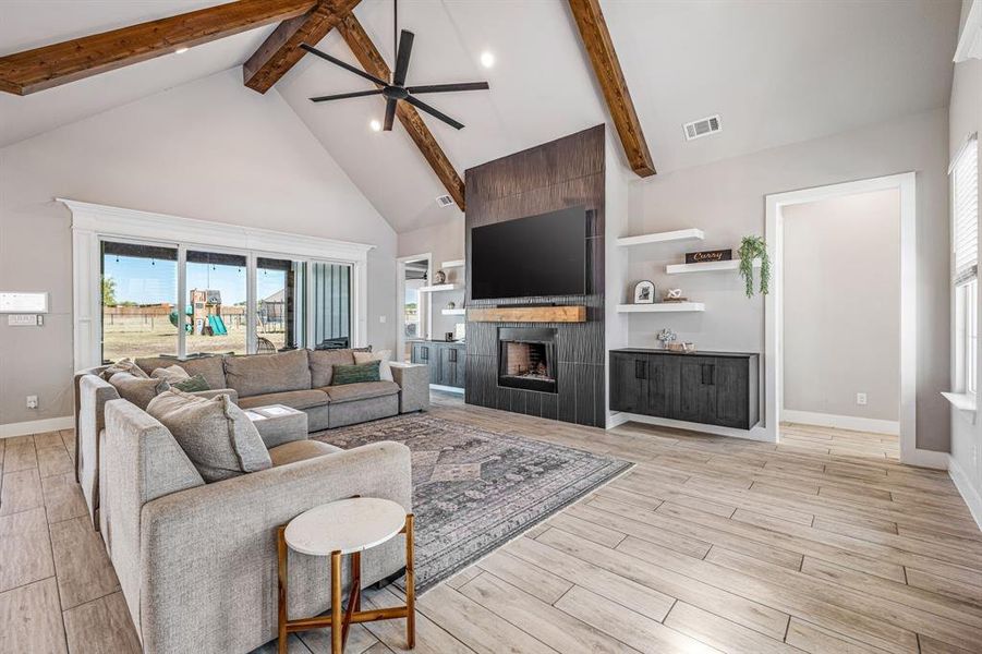 Living area with high vaulted ceiling, a ceiling fan, a fireplace, light wood-type flooring, and beamed ceiling