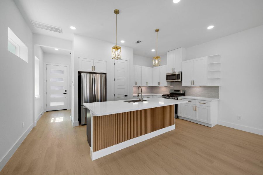 This modern kitchen features sleek white cabinetry, stainless steel appliances, and a large island with a wood accent. Pendant lighting adds a touch of elegance, while the open layout and light wood flooring create a bright and inviting space. This modern kitchen features sleek white cabinetry, stainless steel appliances, and a large island with a wood accent. Pendant lighting adds a touch of elegance, while the open layout and light wood flooring create a bright and inviting space.