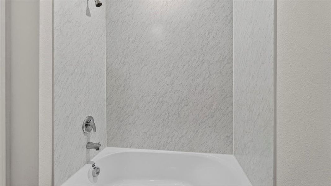 Bathtub and shower combination featuring a white basin, speckled shower surround, and chrome fixtures Bathtub and shower combination featuring a white basin, speckled shower surround, and chrome fixtures