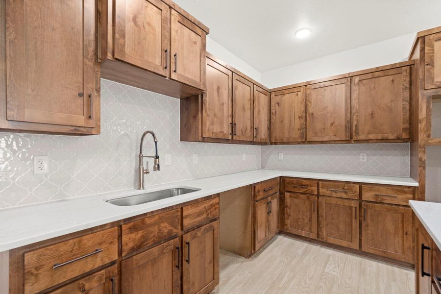 A corner kitchen with light wood cabinetry and a sleek white countertop offers ample prep space.