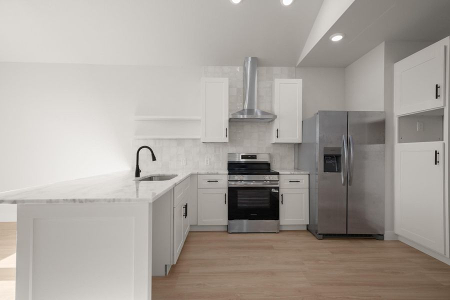 Kitchen featuring a peninsula, stainless steel appliances, light wood-style floors, light stone countertops, and backsplash