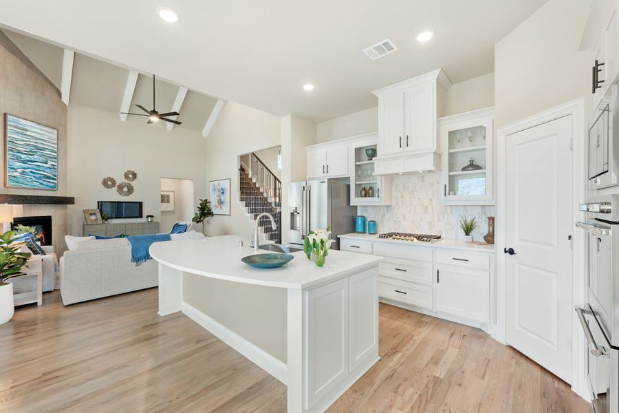 Open-concept kitchen with white cabinets, large island, and hardwood floors open to living room with vaulted ceiling Open-concept kitchen with white cabinets, large island, and hardwood floors open to living room with vaulted ceiling