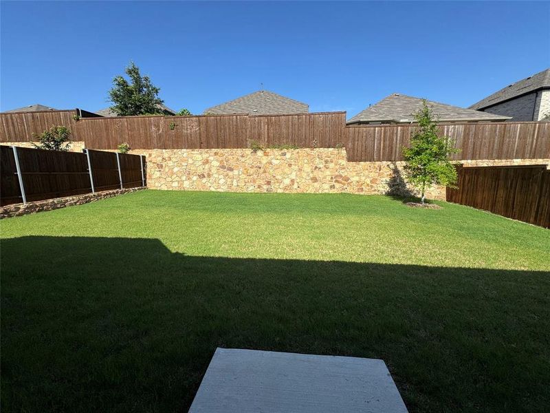 Expansive backyard featuring a large green lawn, stone retaining wall, and wood fencing Expansive backyard featuring a large green lawn, stone retaining wall, and wood fencing
