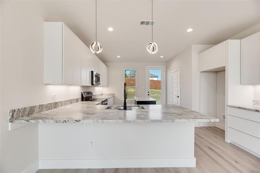 Kitchen with white cabinetry, appliances with stainless steel finishes, light wood finished floors, a peninsula, and pendant lighting Kitchen with white cabinetry, appliances with stainless steel finishes, light wood finished floors, a peninsula, and pendant lighting