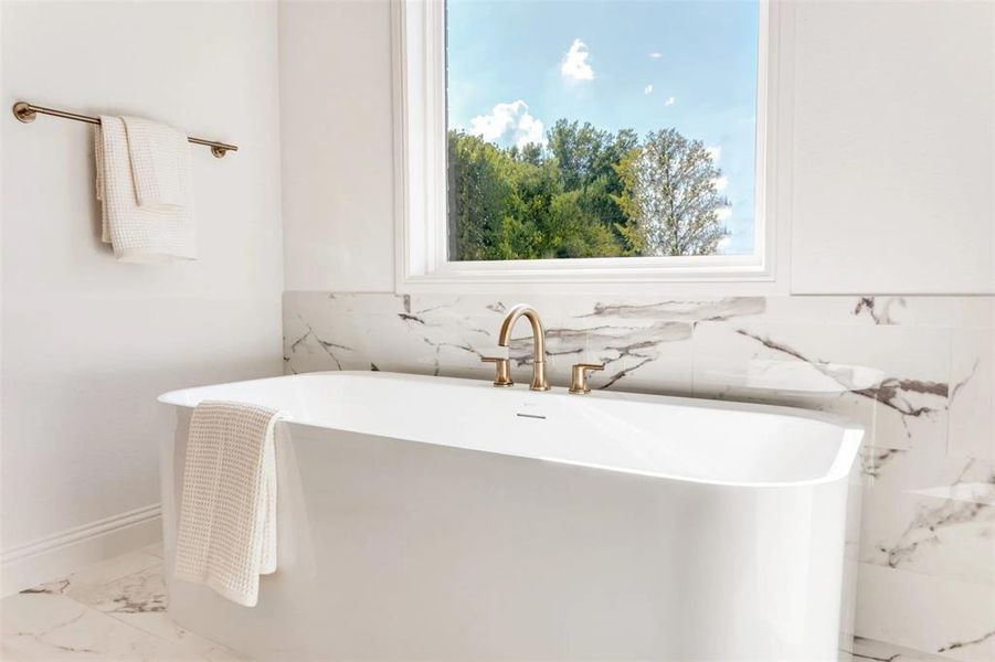Full bath featuring a freestanding tub and light marble finish flooring