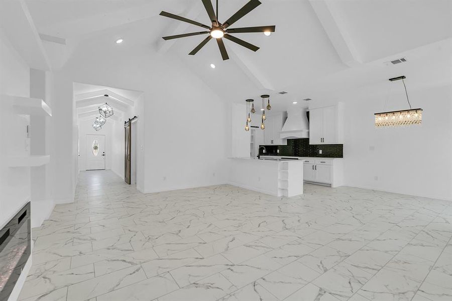 Unfurnished living room with beam ceiling, high vaulted ceiling, ceiling fan with notable chandelier, and light tile patterned floors