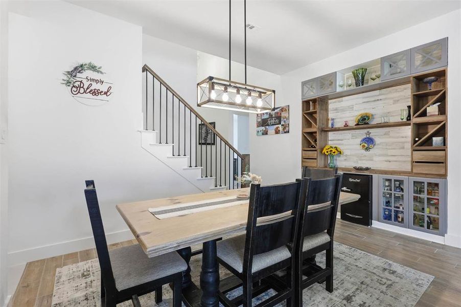 Dining area featuring a wood-finish flooring, a contemporary linear chandelier, and a built-in custom cabinetry unit with integrated shelving, wine racks, and glass-front doors