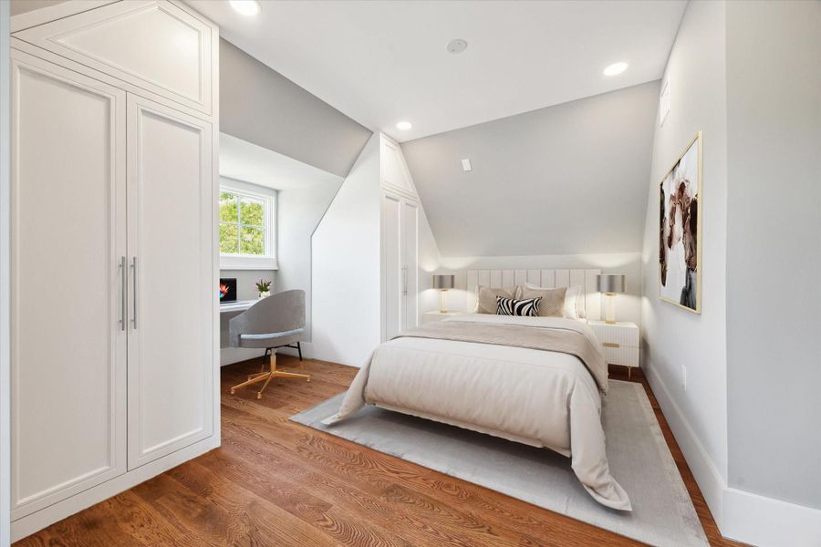 This is a cozy, modern bedroom on the 3rd floor with a sloped ceiling, featuring a comfortable bed, wood flooring, and a small workspace by a window. The room is bright, thanks to recessed lighting and neutral tones, creating a warm and inviting atmosphere.  This photo has been virtually staged.