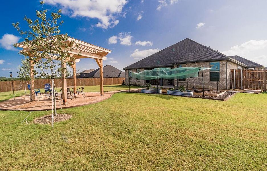 Expansive backyard featuring a covered patio extended to a wooden pergola living space, vegetable garden, a large grassy area, and a privacy fence.