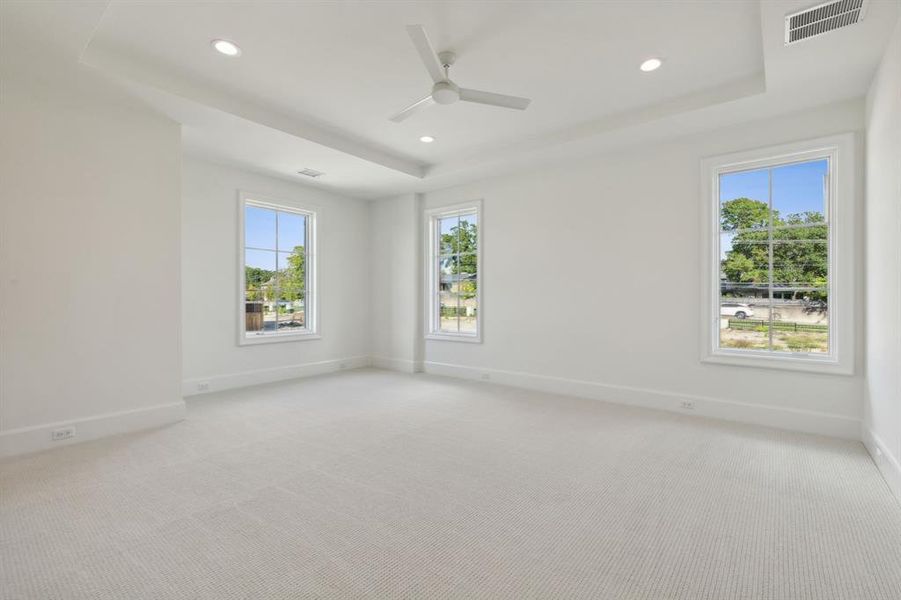 Bedroom with ceiling fan, light colored carpet, a tray ceiling, and a wealth of natural light