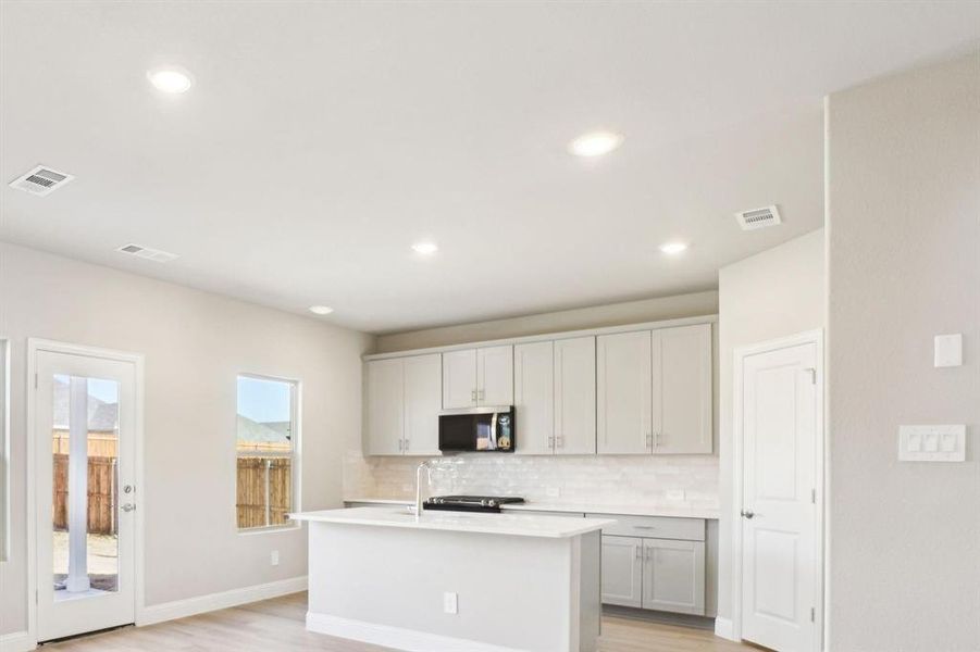 Kitchen with tasteful backsplash, light wood-type flooring, a center island with sink, black microwave, and recessed lighting Kitchen with tasteful backsplash, light wood-type flooring, a center island with sink, black microwave, and recessed lighting