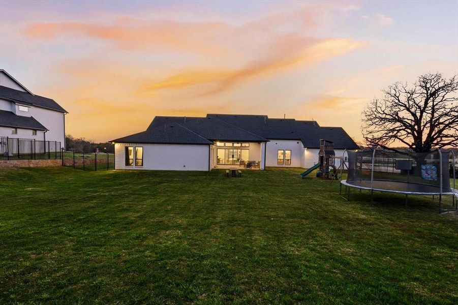 Back of house at dusk with a patio, a trampoline, and a playground