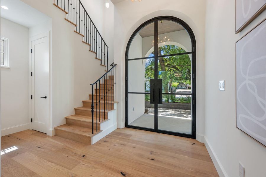 An arched glass entry door frames garden views from the hardwood foyer.