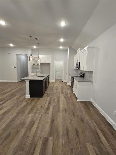 Kitchen with dark wood-type flooring, hanging light fixtures, electric range, and an island with sink