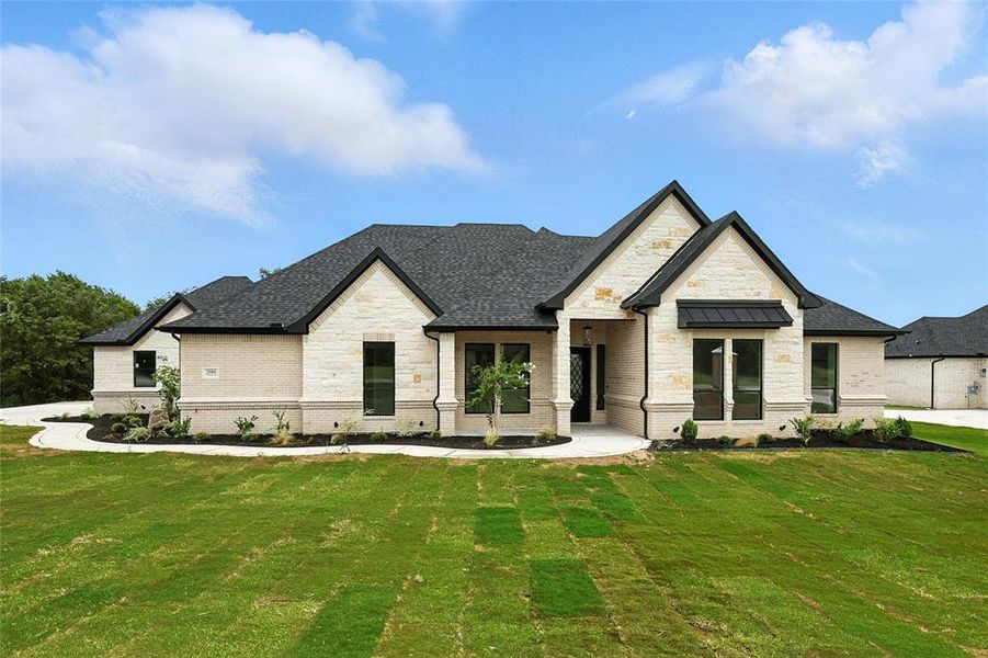 French country style house with stone siding, a front lawn, brick siding, and roof with shingles