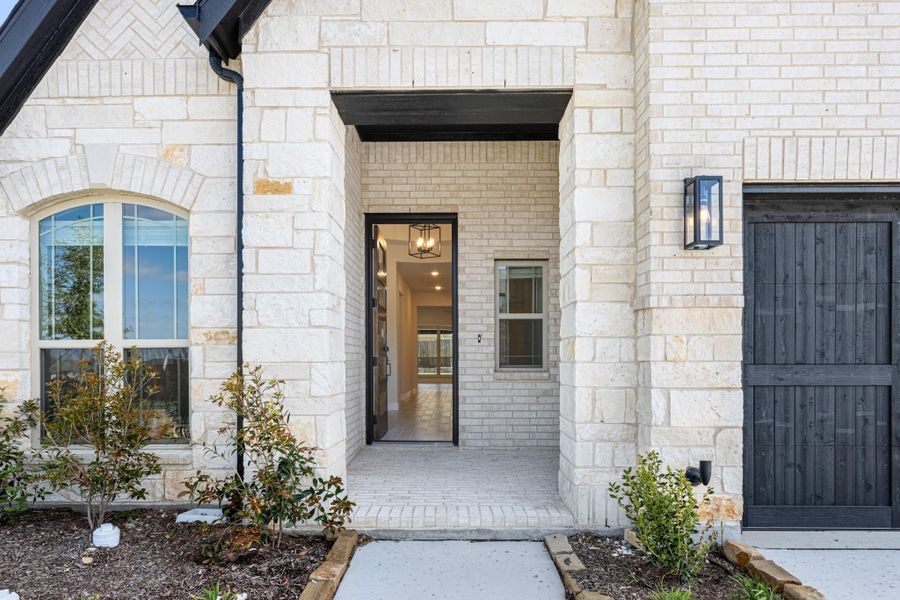 Home entrance with cream stone exterior, open glass front door, and black wall sconce light fixture Home entrance with cream stone exterior, open glass front door, and black wall sconce light fixture
