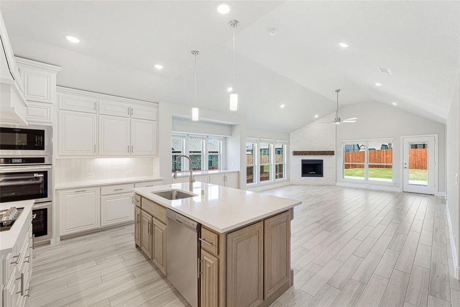 Open kitchen with center island, white cabinets, stainless appliances, and vaulted ceiling open to living room with fireplace.