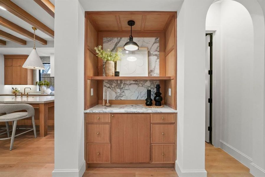 Bar area with brown cabinetry, light wood-style floors, light stone counters, open shelves, and beamed ceiling Bar area with brown cabinetry, light wood-style floors, light stone counters, open shelves, and beamed ceiling